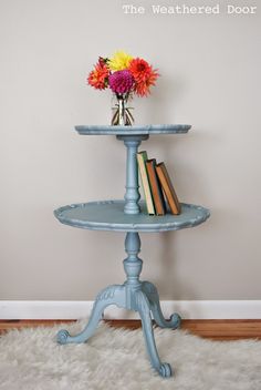 a blue table with books and flowers on it in front of a white wall that says the weathered door