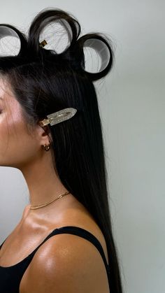 a woman with long black hair has some scissors in her hair and is wearing ear clips