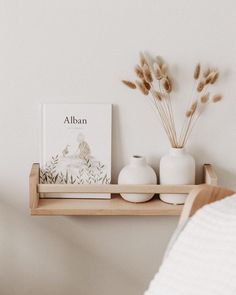 two white vases are sitting on a shelf next to a book and an art print