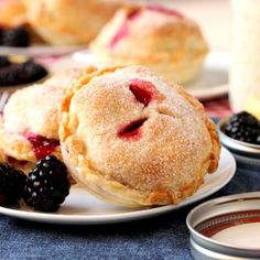 two small pies on a plate with berries and blueberries next to some fruit