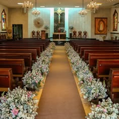 an empty church filled with wooden pews and flower arrangements on either side of the aisle