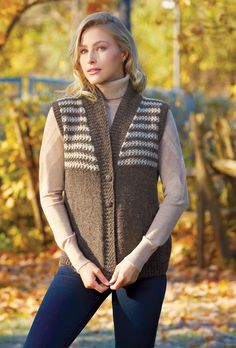 a woman wearing a sweater vest and leggings stands in front of trees with leaves