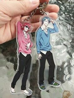 two anime key chains with one being holding the other's head and another is wearing a pink shirt