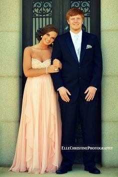 a young man and woman standing in front of a door wearing formal wear, smiling at the camera