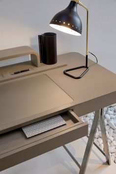 a desk with a lamp on top of it next to a pile of rocks and paper