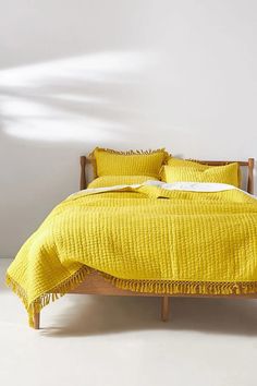 a bed with yellow sheets and pillows in a white room, next to a wooden headboard