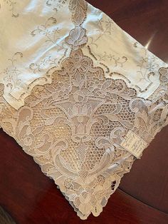 an old lace tablecloth on a wooden table with a tag in the middle of it