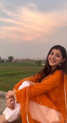 a woman in an orange outfit is sitting on a ledge and smiling at the camera