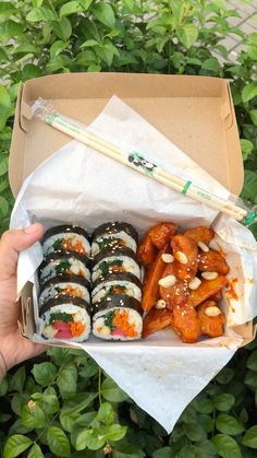 someone holding up a box full of sushi and chopsticks