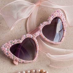 a pair of pink sunglasses with pearls on them and a beaded bracelet next to it