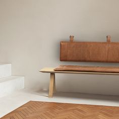 a brown leather bench sitting on top of a wooden floor next to a white wall