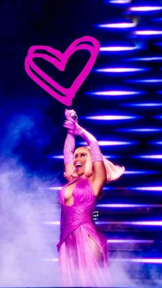 a woman in a pink dress is holding a heart shaped object above her head on stage