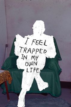 a man sitting in a chair with a sign on it that says i feel trapped in my own life