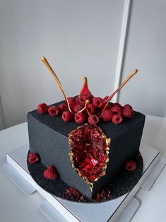 a black cake with raspberries on top and gold decoration around the edges is sitting on a white table