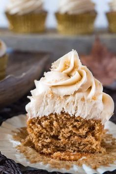 a piece of carrot cake with cream frosting on a plate next to a cupcake