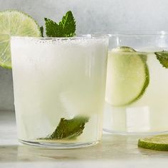 two glasses filled with lemonade and limes next to each other on a counter