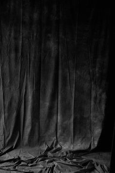 a black and white photo of an unmade bed with sheets on the floor in front of a curtain