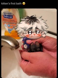 a person holding a small toy in their hand next to a sink with soap on it