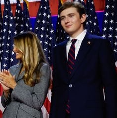 two people standing next to each other in front of american flags