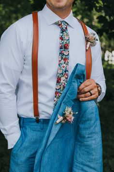 a man wearing suspenders and a tie with flowers on it is holding his jacket