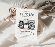 a monster truck birthday party card sitting on top of a white sheet with feathers in the background