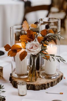 two vases filled with flowers and candles on top of a wooden slice at a table