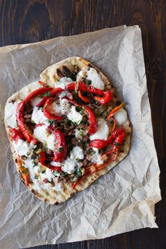 an uncooked flatbread with peppers, cheese and herbs on parchment paper sitting on a wooden table