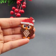 an owl beaded brooch sitting on top of someone's hand in front of a christmas tree