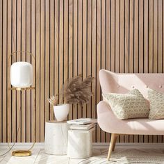 a pink chair with two pillows on it next to a white lamp and wooden wall