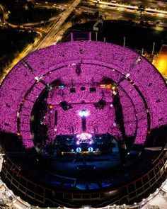 an aerial view of a concert venue at night with the lights on and purple flowers in the center