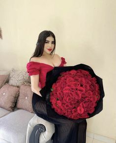 a woman is sitting on a couch holding a large bouquet of roses in her hands