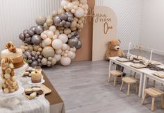 a teddy bear sitting in front of a table filled with cake and desserts next to balloons