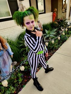 a young boy dressed as beetle costume standing in front of a house with green hair and makeup