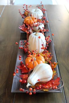 some pumpkins and gourds are sitting on a tray with leaves, berries and acorns