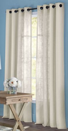 a living room with blue walls and white drapes on the windowsill, along with a small wooden table