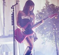 a woman in short skirt and boots holding a guitar on stage with microphones behind her