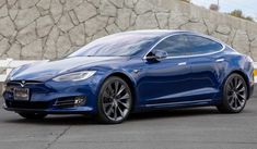 a blue tesla parked in front of a stone wall