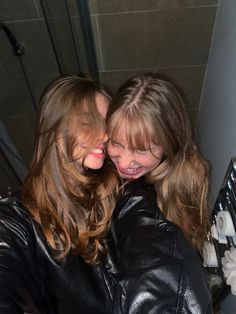 two young women are hugging each other in the bathroom, one is wearing a black leather jacket