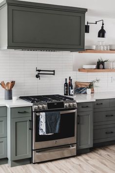 a kitchen with gray cabinets and stainless steel stove top, white subway backsplash