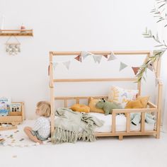 a little boy sitting on the floor in front of a bed with pillows and blankets