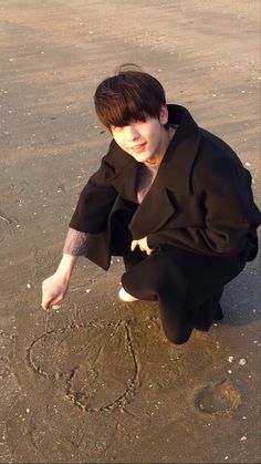 a young man kneeling on top of a sandy beach next to the ocean writing in the sand