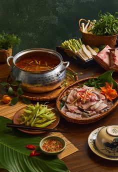 a table topped with bowls filled with food next to green plants and other foods on plates