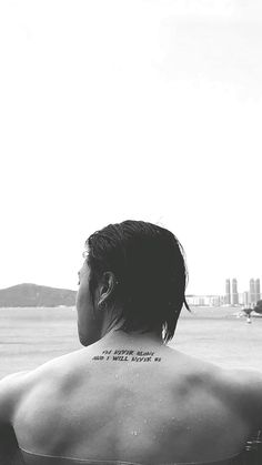 a woman with a tattoo on her back looking out over the water at an airplane