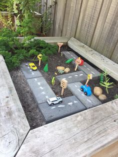 an outdoor play area with toy cars and toys in the dirt, surrounded by wooden fence