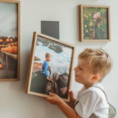 a little boy holding up some pictures on the wall