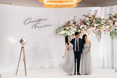 a man and two women standing in front of a floral display at a fashion show