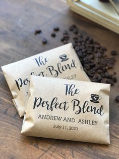 two bags of coffee beans sitting on top of a wooden table next to some coffee beans