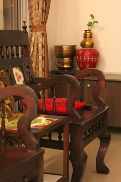 a wooden chair sitting in front of a window next to a red vase on a table