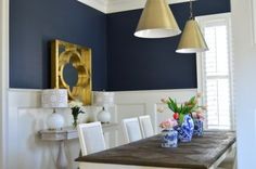 a dining room table with white chairs and blue walls in the background, along with two gold pendant lights