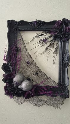 an old frame is decorated with purple and black yarn, spider webs and skulls